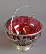 CRANBERRY GLASS SUGAR BASIN IN A SWING HANDLED WIRE PATTERN UNMARKED SILVER HOLDER, of cylindrical
