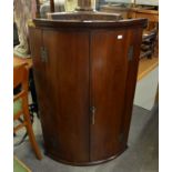 A MAHOGANY BOW FRONTED MURAL CORNER CUPBOARD, WITH TWO DOORS, THE INTERIOR WITH SMALL DRAWERS AND