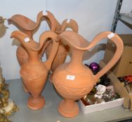 FOUR TERRACOTTA LARGE EWERS IN SIZES, WITH EMBOSSED FOLIATE GIRDLES, RAISED ON CIRCULAR PLINTH