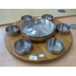 A STAINLESS STEEL LAZY SUSAN, WITH SIX SMALL BOWLS ROUND A CENTRE LARGE BOWL, ON TEAK REVOLVING BASE