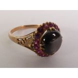 BLACK STAR SAPPIRE AND RUBY CLUSTER RING, an oval black star sapphire within a border of rubies,