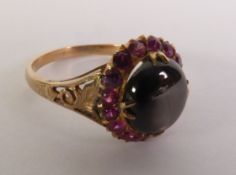 BLACK STAR SAPPIRE AND RUBY CLUSTER RING, an oval black star sapphire within a border of rubies,