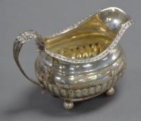 GEORGE IV SILVER CREAM JUG of rounded-oblong form with gadrooned rim and demi-gadrooned body, with