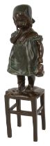 A bronze figure of a young girl standing on a stool