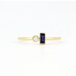 An 18ct yellow gold (stamped 750) ring set with a baguette cut sapphire and a brilliant cut diamond,