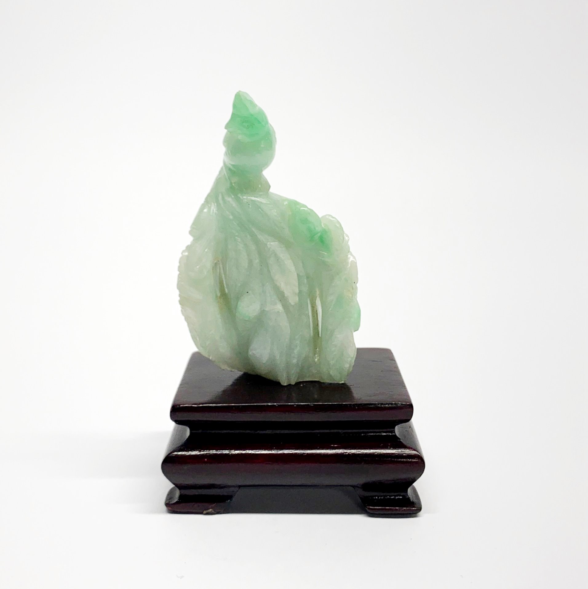 A Chinese carved jade model of a bird resting on a branch with carved wooden stand, overall H. 9cm.