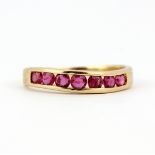 A 14ct yellow gold ring channel set with round cut rubies, (L.5).