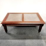 A carved hardwood coffee table on castors with cane decoration and plate glass coverings, 127 x 76 x