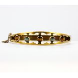 An antique yellow metal (tested 15ct gold) bangle set with tiger's eye and cat's eye chrysoberyl, L.