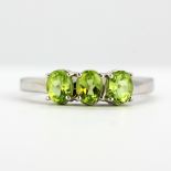 A 9ct white gold ring set with three oval cut peridots, (M).