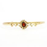 A 9ct yellow gold bangle set with an oval cut garnet, L. 6.5cm. Slightly bent.