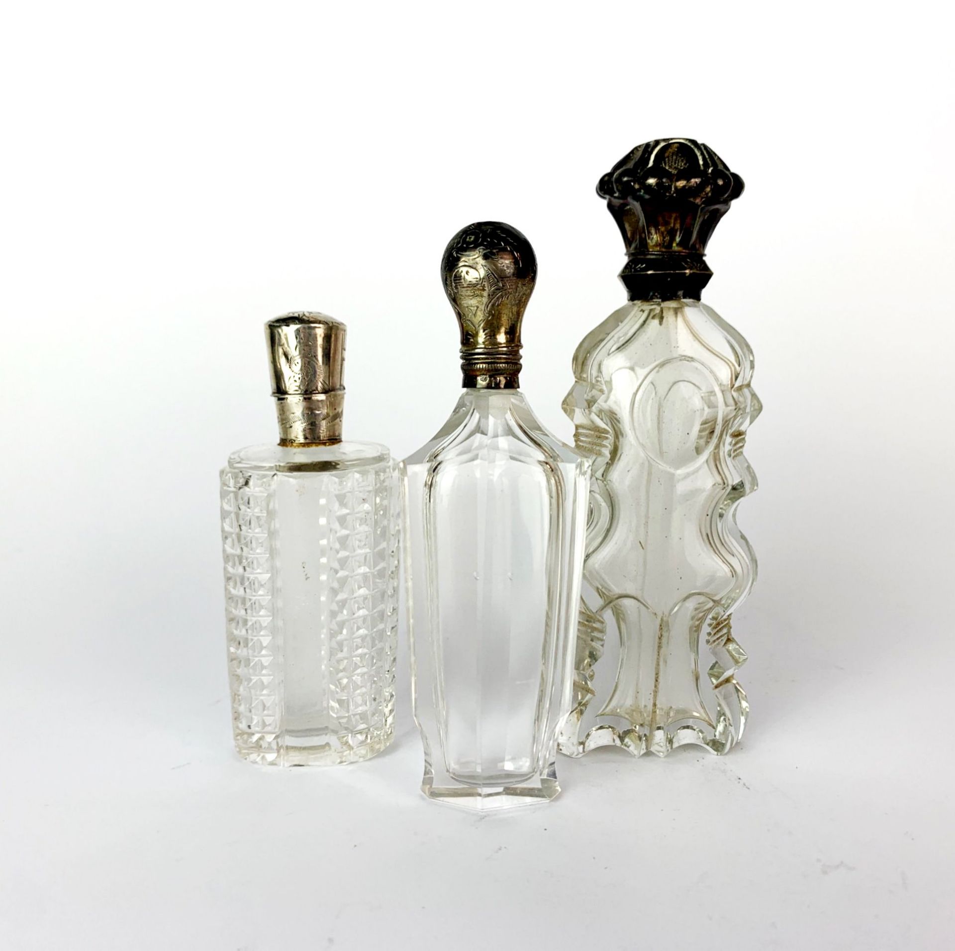 Three antique cut glass and silver topped (tested) perfume bottles, tallest H. 12cm.