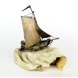 An antique handmade white metal sailing vessel mounted on a section of fossilized jaw bone, W.