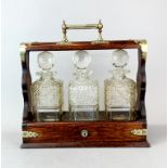 An oak and brass cased three bottle tantalus, W. 36cm. H. 35cm. one bottle is A/F to rim.