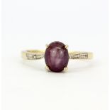 A hallmarked 9ct yellow gold ring set with an oval cabochon ruby and diamond set shoulders, (S).