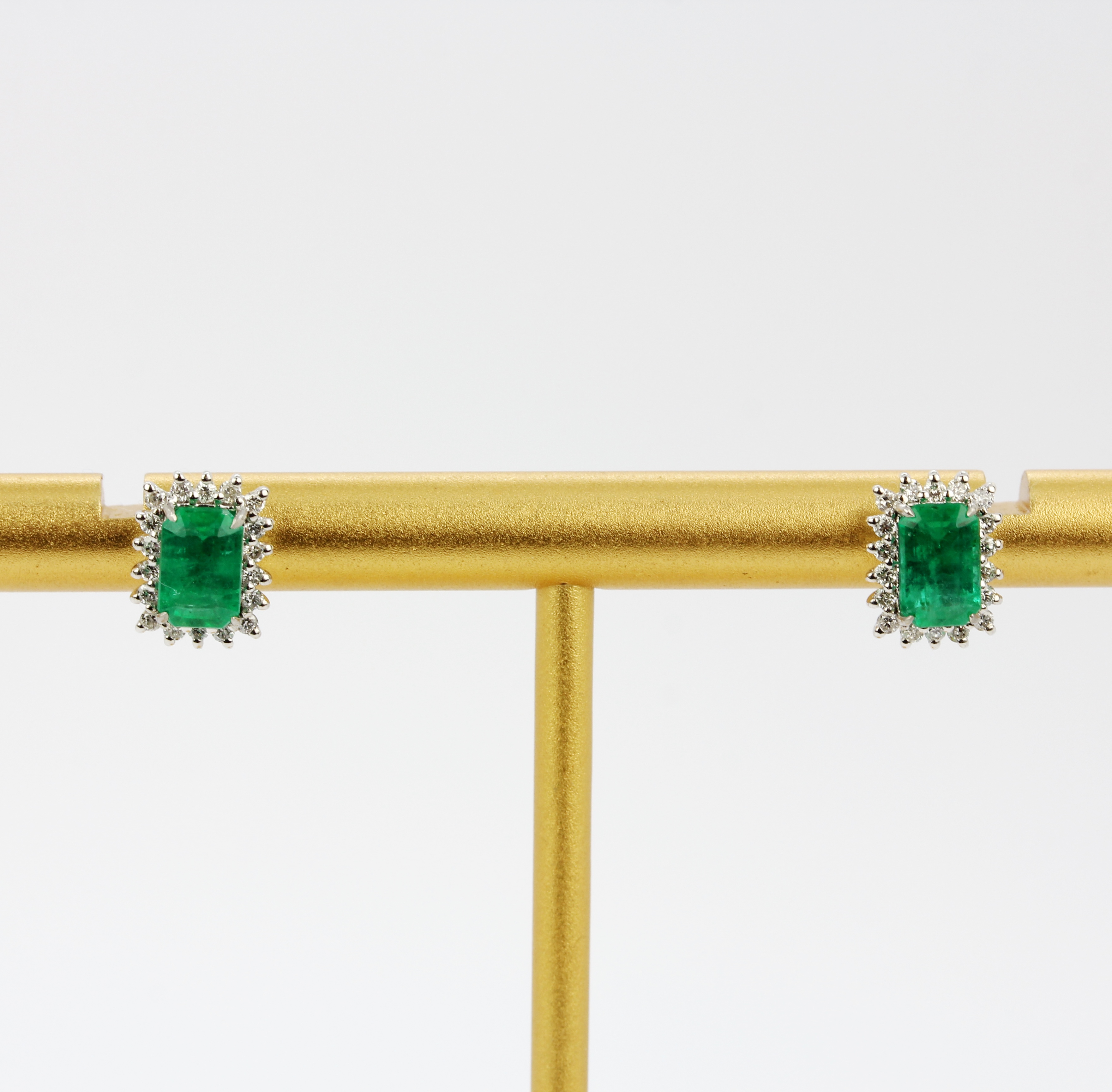 A pair of 18ct white gold stud earrings each set with an emerald cut emerald surrounded by brilliant