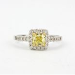A white metal (tested high carat gold) ring set with a cushion cut fancy yellow diamond surrounded