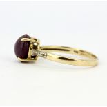 A hallmarked 9ct yellow gold ring set with an oval cabochon ruby and diamond set shoulders, (S).