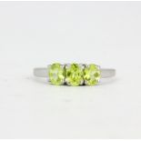 A hallmarked 9ct white gold ring set with three oval cut peridots, (O).