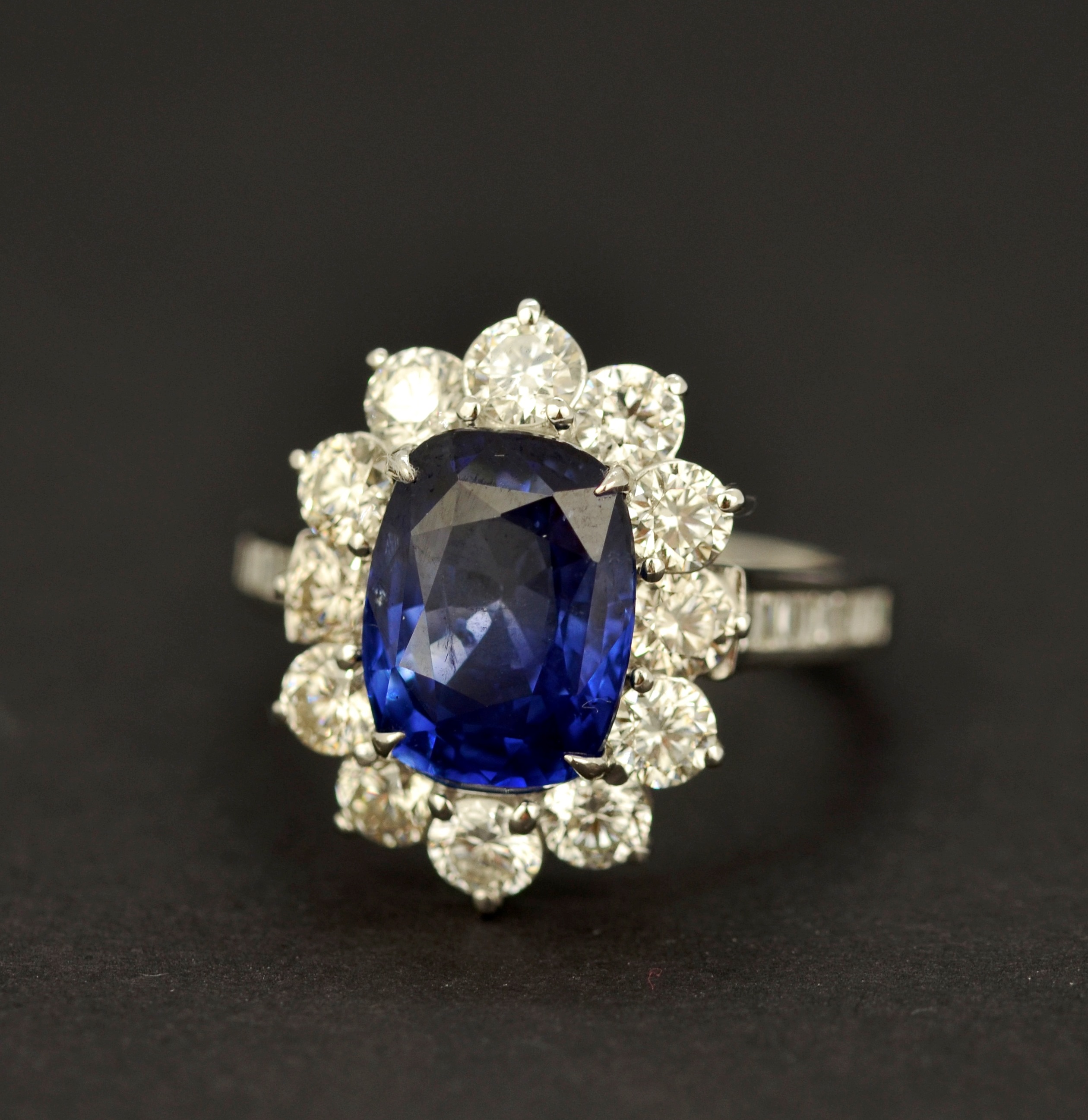 An 18ct white gold cluster ring set with a large cushion cut sapphire, approx. 4.52ct, L. 1.2cm,