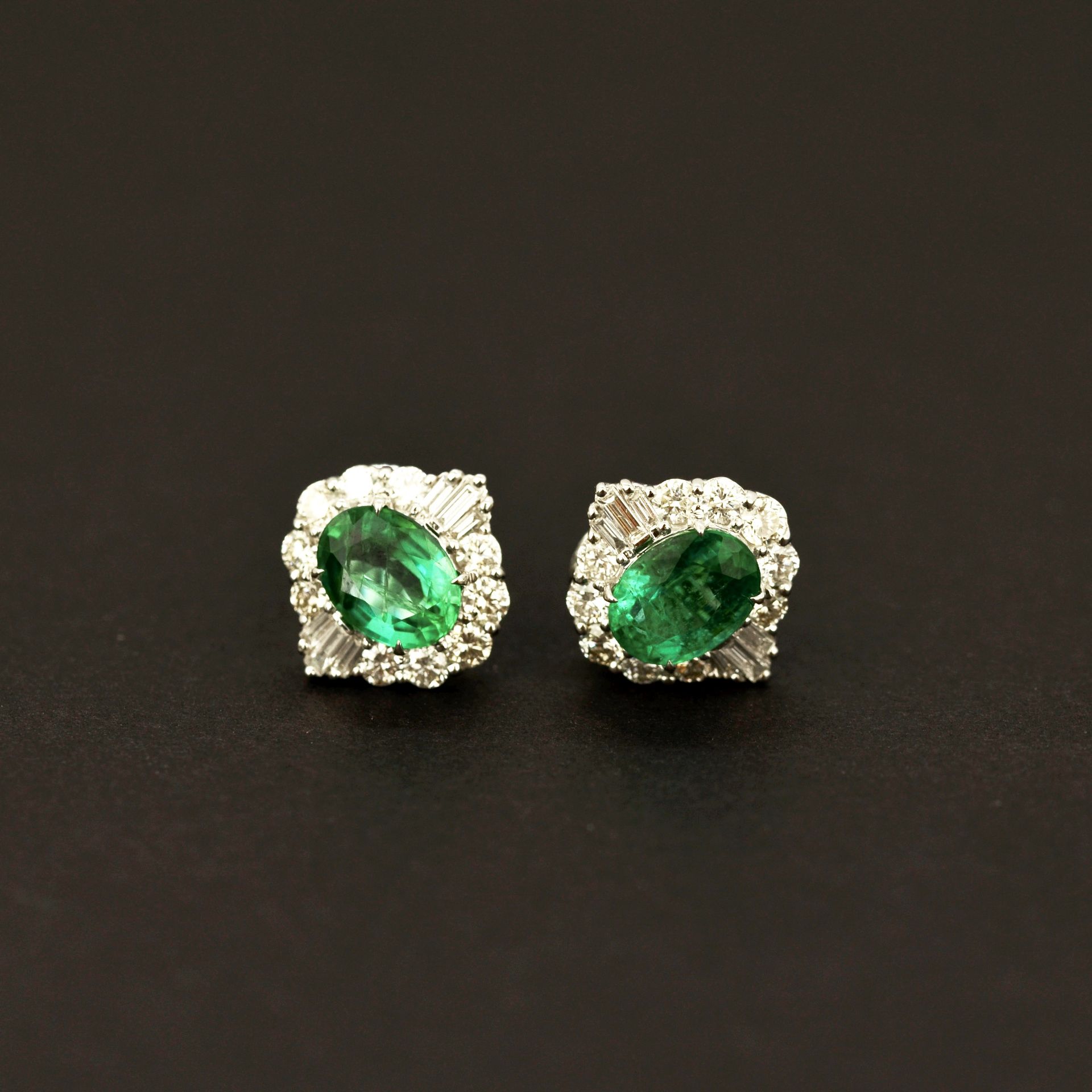 A pair of 18ct white gold stud earrings set with oval cut emeralds, approx. 2.64ct total, surrounded