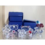 A group of Swarovski crystal bear figures with a vase of flowers, three with boxes.