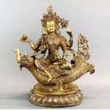 A Tibetan gilt bronze figure of a multi armed goddess seated on a mythical sea creature, H. 26cm.