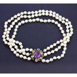 A triple strand cultured pearl necklace with a clasp set with a large oval cut amethyst surrounded