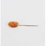 An antique yellow metal (tested minimum 9ct gold) and carved coral topped stick pin, L. 7cm.