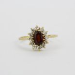 A hallmarked 9ct yellow gold cluster ring set with an oval cut garnet surrounded by white stones, (