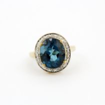 A hallmarked 9ct yellow gold ring set with a large oval cut blue topaz, L. 1.1cm, surrounded by