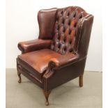 An oxblood red leather chesterfield wingback armchair, H. 106cm.