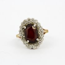 A hallmarked 9ct yellow gold ring set with an oval cut garnet surrounded by diamonds, (J).