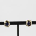 A pair of 18ct yellow and white gold (stamped 750) earrings set with oval cut sapphires surrounded
