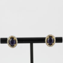 A pair of 18ct yellow and white gold (stamped 750) earrings set with oval cut sapphires surrounded