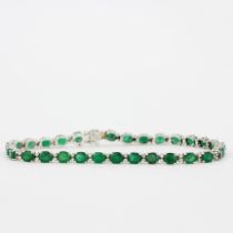 An 18ct white gold (stamped 750) tennis bracelet set with oval cut emeralds and brilliant cut