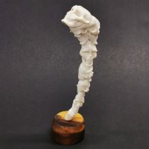 A hand carved antler tine in the form of seven stacked human skulls on a hardwood base.