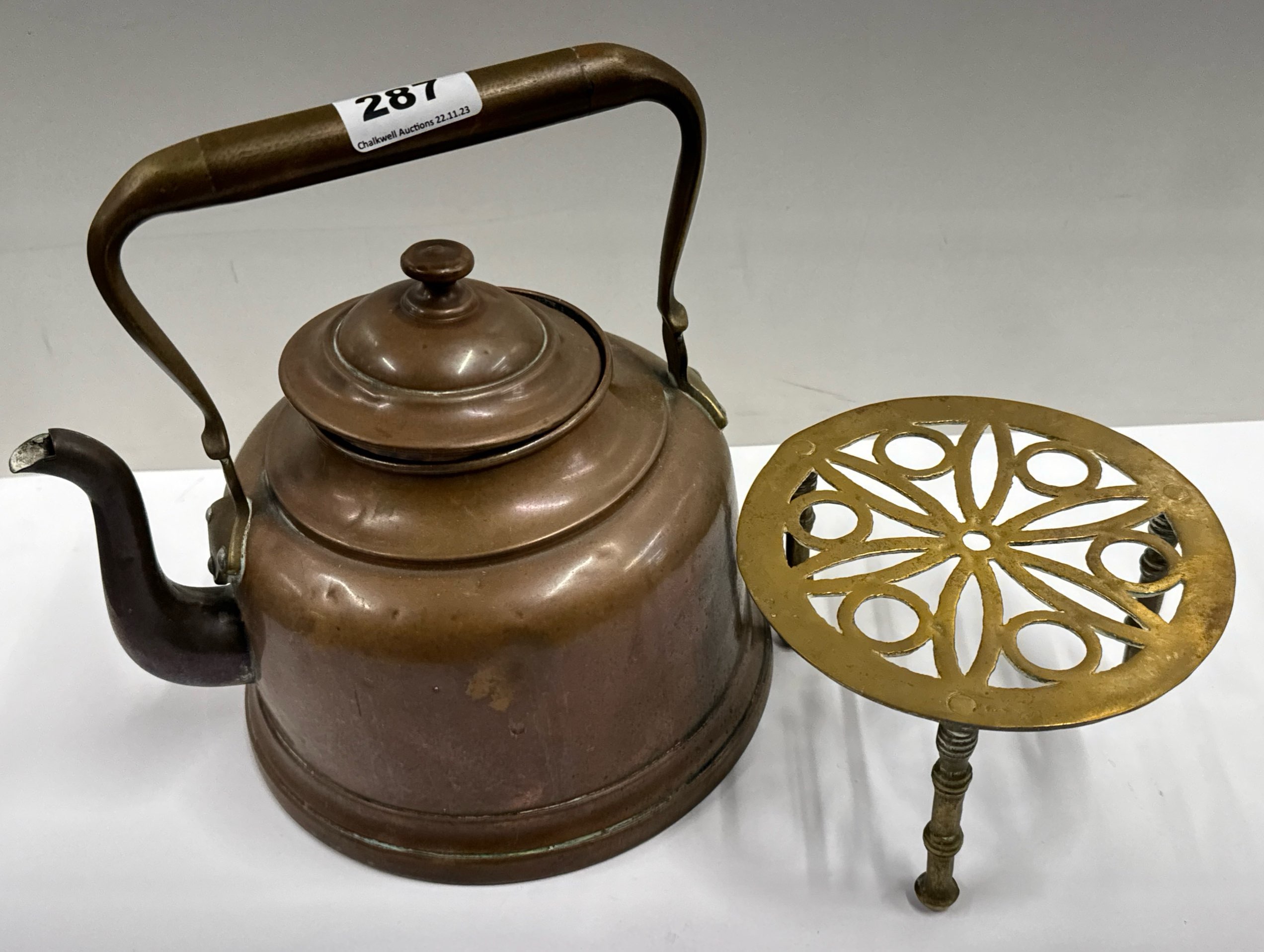 A copper kettle and brass trivet.