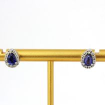 A pair of 18ct white gold stud earrings each set with a pear cut sapphire surrounded by brilliant