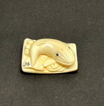 A carved fossilised mammoth tusk signed Netsuke of a whale, 3 x 2cm.