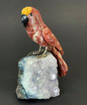 A hand carved jasper Parrot with white metal legs sat on top of a rough amethyst with carved black