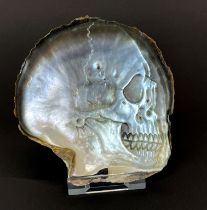 A hand-carved black-lip oyster mother of pearl shell with skull with Perspex display stand, H.