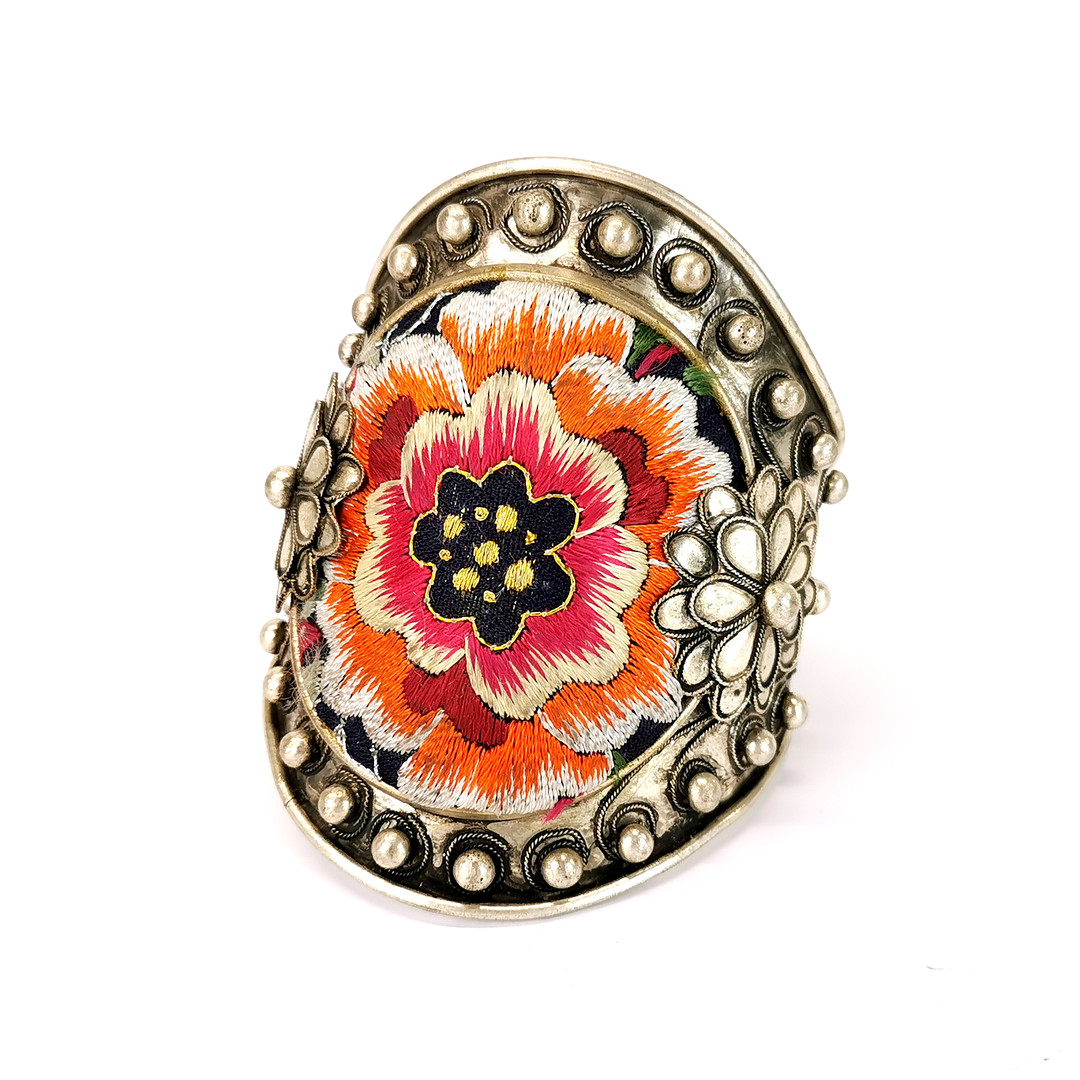 A Chinese white metal bangle inset with tribal embroidered fabric, top W. 9cm.