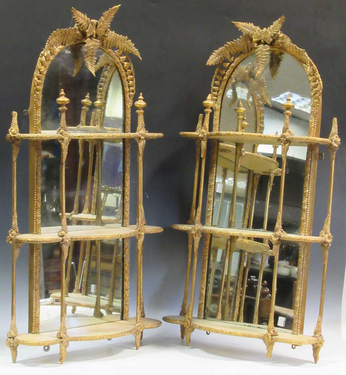 A near pair of Victorian gilt wall-mounted mirror backed etageres, with fern leaf crests and three