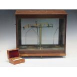 Scales within a glazed case together with weights in a smaller wooden box, 42 x 46 x 24cm