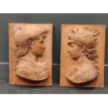 A pair of terracotta plaques depicting relief profile busts of a man and woman in classical dress,