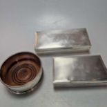 Two silver table cigarette boxes together with a silver bottle coaster (3)