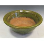A large earthenware bowl partially covered in green lead glaze and having applied motifs, 52cm