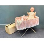 A 1930s composition doll with spare clothing and draped cradle