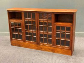 A late Victorian walnut panel glazed four door bookcase with open shelves attributed to Jas